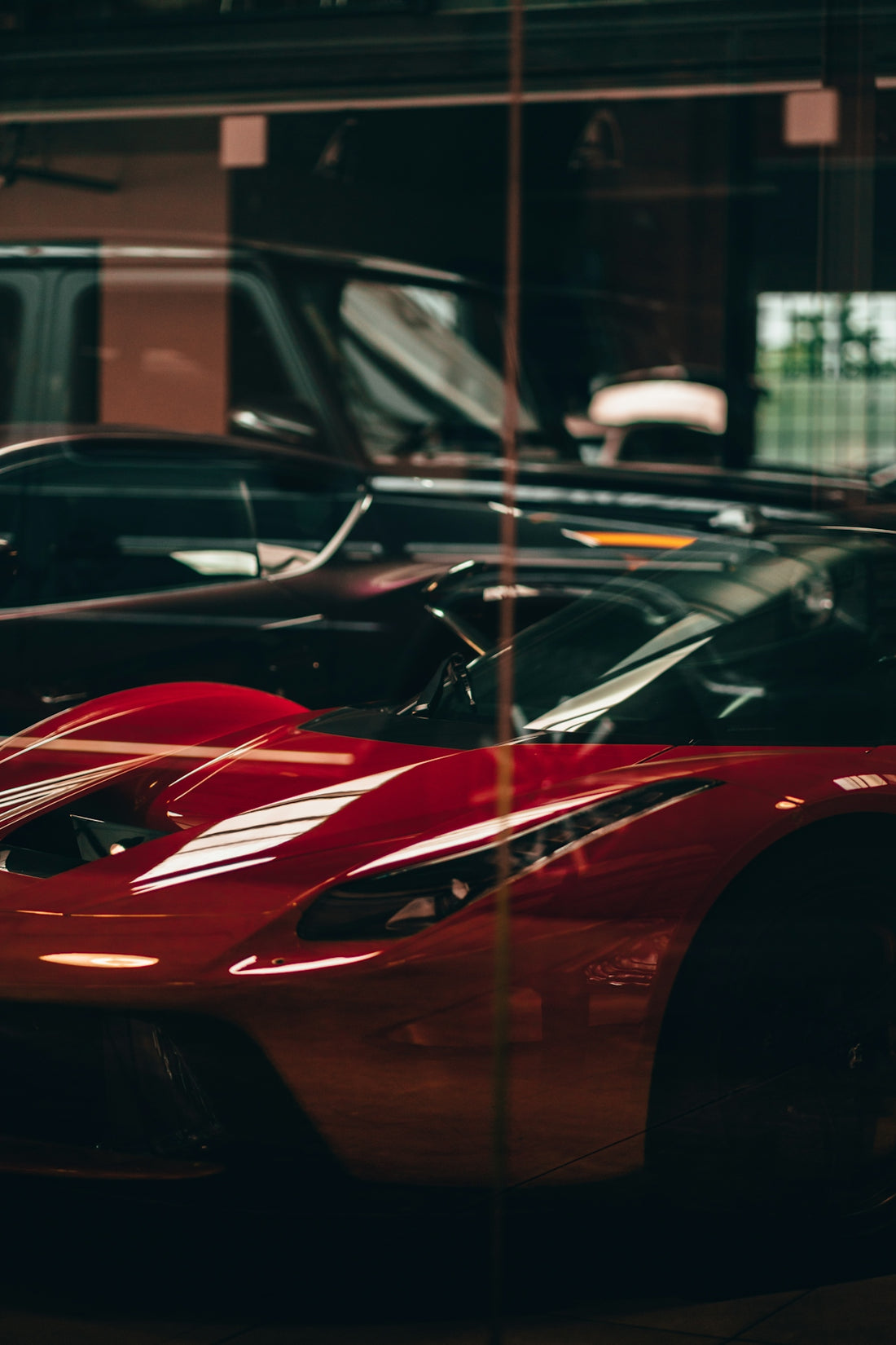 Red sports car reflected in glass with other cars