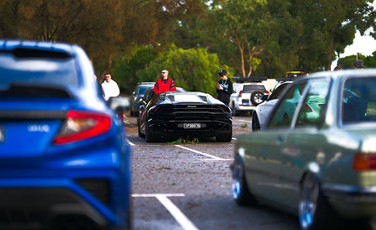 Black sports car surrounded by people and other vehicles