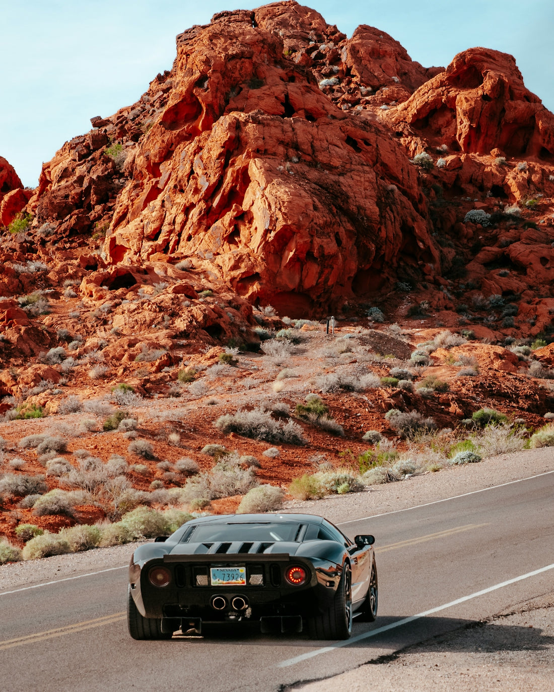 A black sports car driving on a desert road past red sandstone rock formations